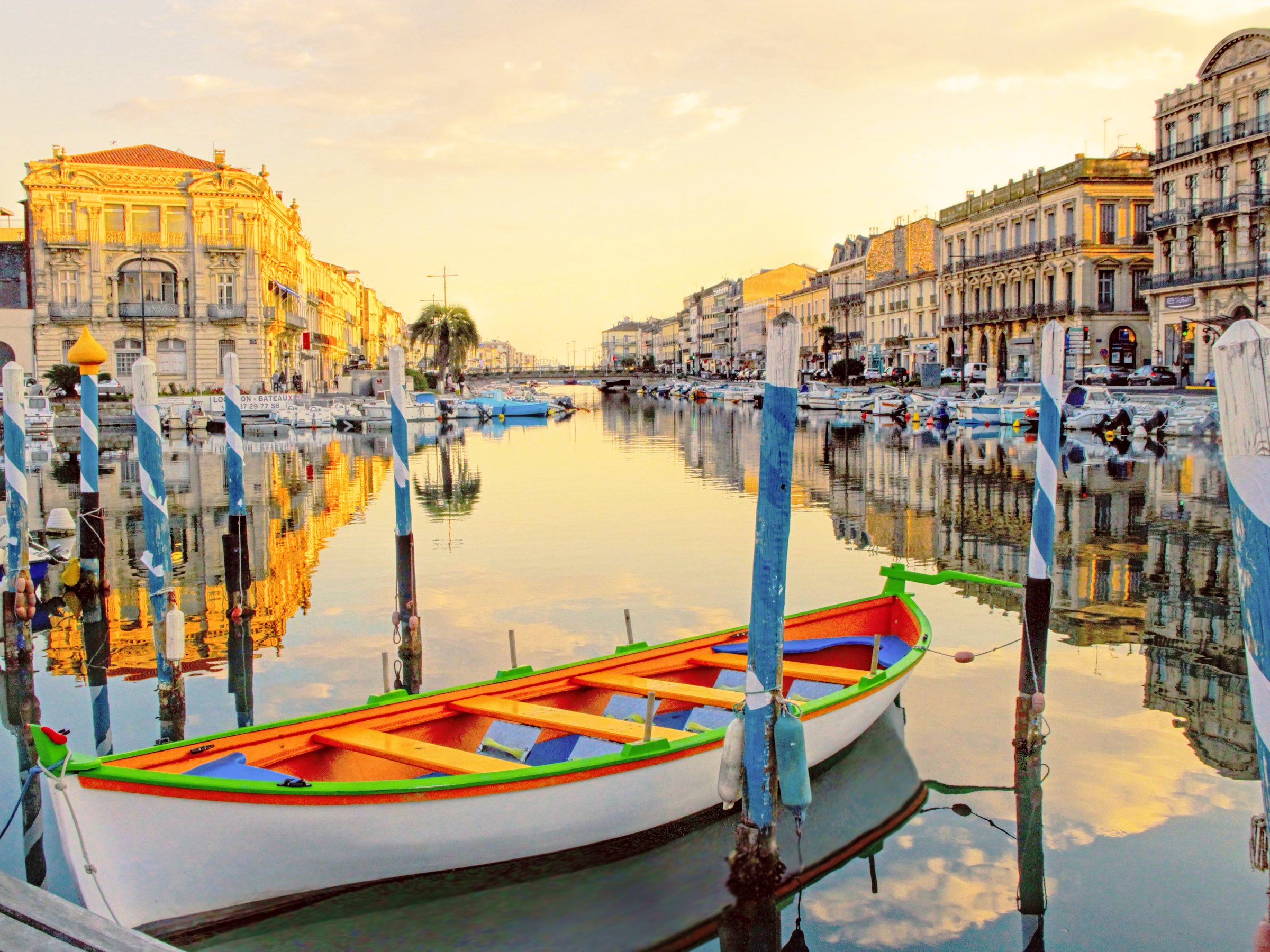 Des barques traditionnelles amarrées dans un canal de Sète, devant les façades du quai