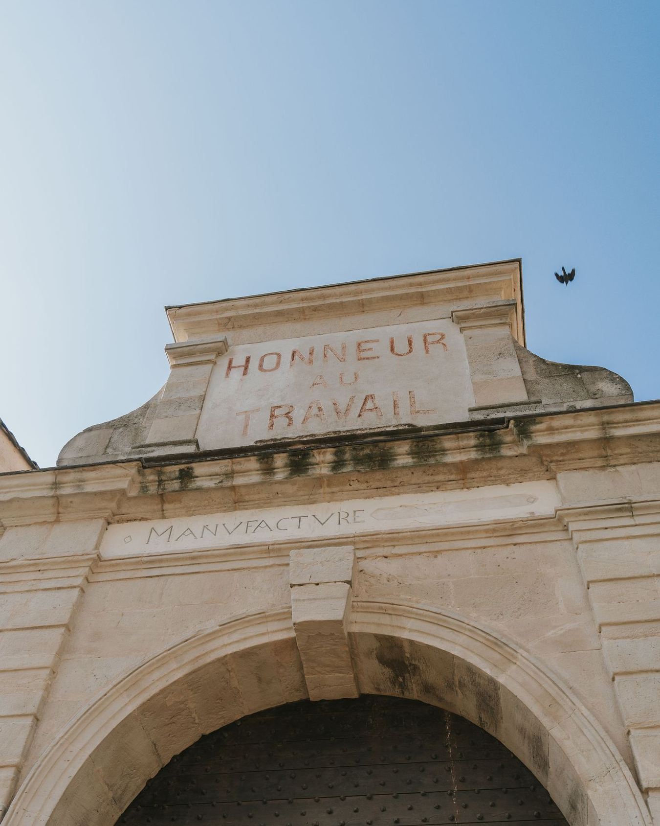 La porte de la manufacture de Villeneuvette, « Honneur au travail » gravé dans le fronton au-dessus de l’arche