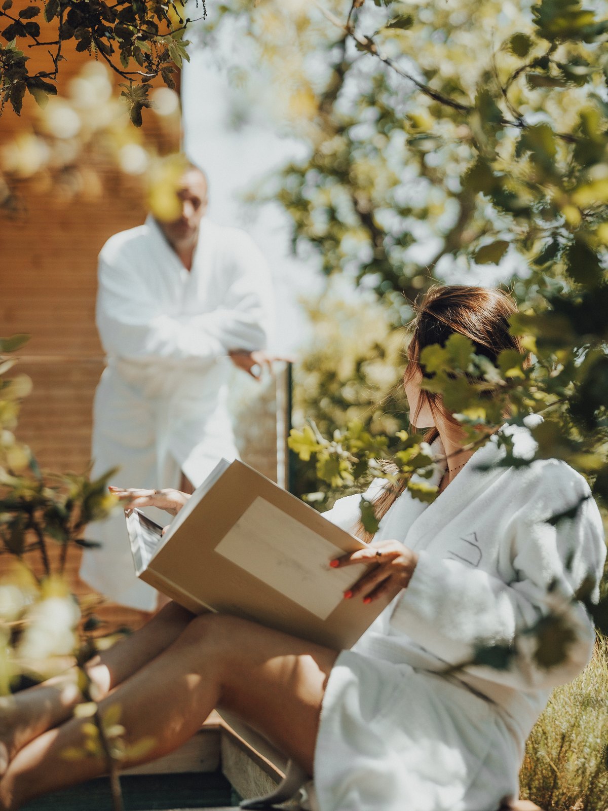 Deux voyageurs en peignoir lisant sous les chênes du domaine, Souki Lodges & Spa (Hérault)