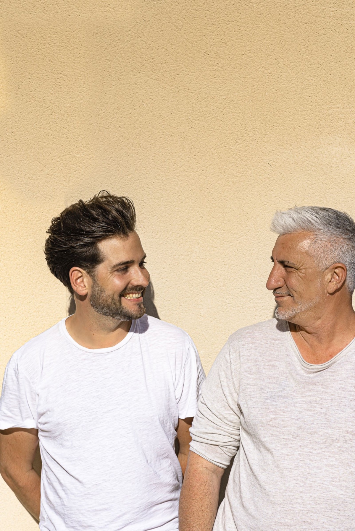 Gilles et Fabien échangent un regard complice devant un mur ocre