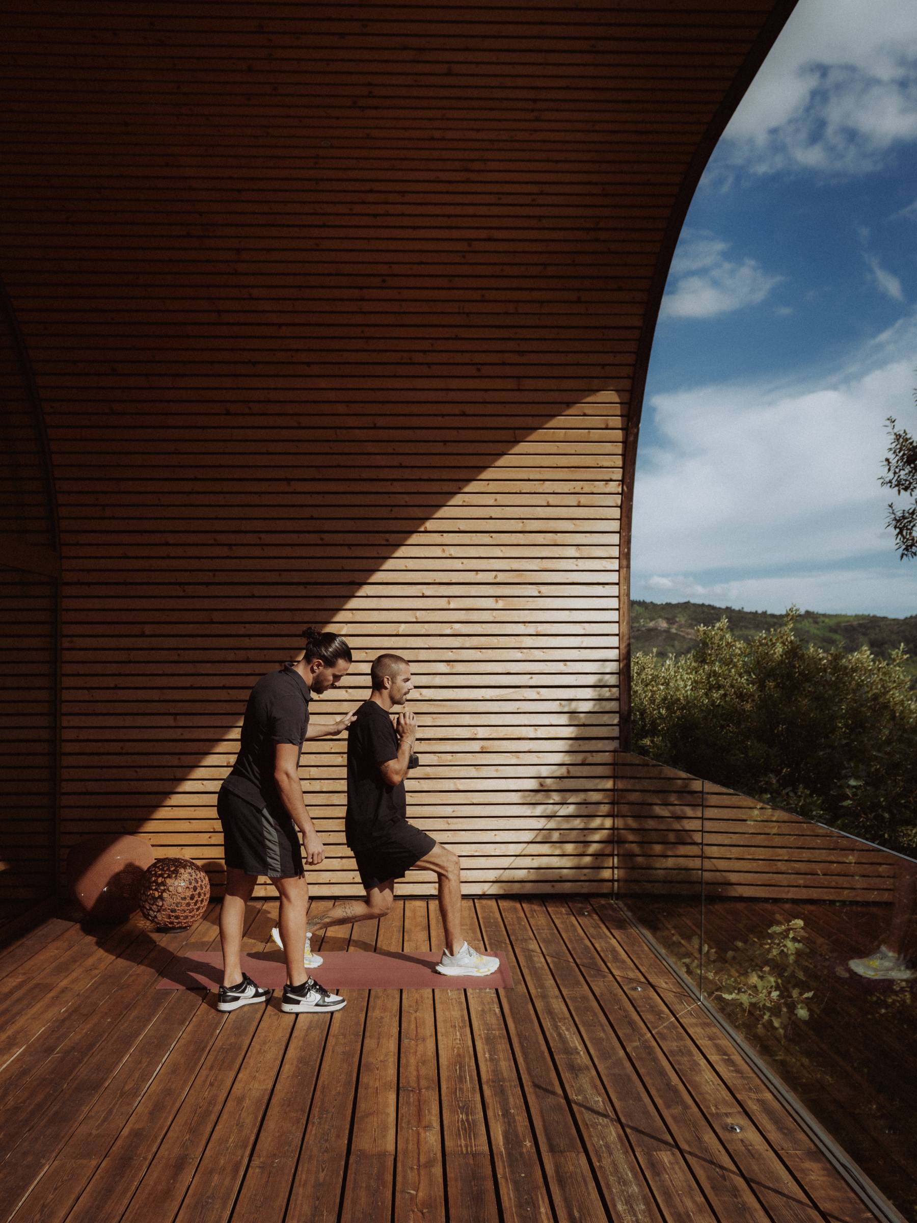 Fentes le long du mur de bois de la terrasse, le coach accompagne le mouvement