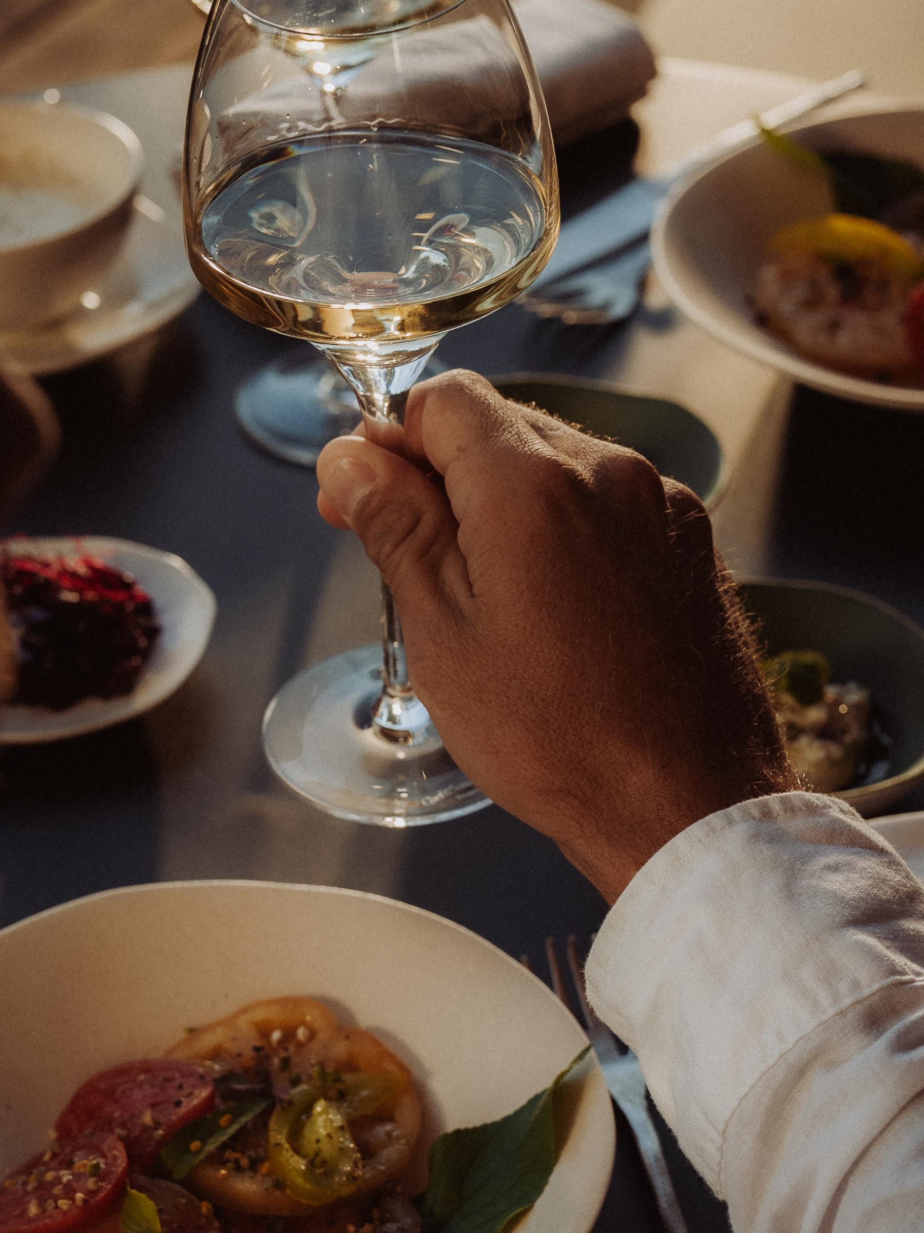 Table du soir : une main lève un verre de vin blanc au-dessus des assiettes